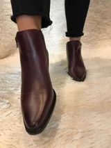 Botín de cuero color borgoña, con punta fina, cierre lateral y taco bajo de madera.
