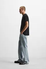 Pantalón de jean negro con efecto lavado, corte flare, cinco bolsillos, cierre frontal con cremallera y botón, y bajo con acabado irregular.
