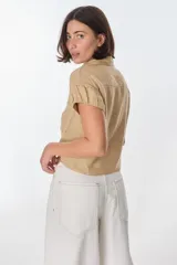 Camisa color beige de lino, con cuello clásico, manga corta con detalle de frunce y bolsillo de parche en el pecho.