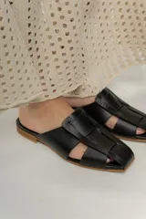 Zuecos negros con diseño de tiras entretejidas y suela plana color madera.