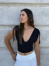 Top corto negro con lunares blancos, escote en V, mangas cortas con lazos en los hombros y corte ajustado.