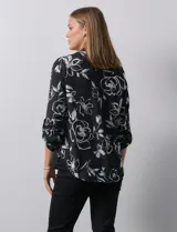 Blusa de gasa estampada con flores blancas sobre fondo negro, marca Floral & Ivy. Tiene cuello a la base con escote en V y mangas tres cuartos regulables con presilla y botón.