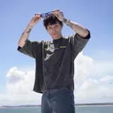 Remera de algodón 100% color gris oscuro con efecto acid washed. Estampa grande en la espalda con el logo "Venefo" en amarillo y texto en blanco que incluye "Industries Company \ 004®1994" y "Worldtribe Co".