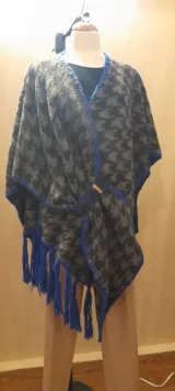 Ruana artesanal con diseño de patchwork en la espalda, terminación de pespuntes y crochet en lana con flecos azules.