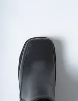 Bota corta tipo Chelsea de cuero negro, con puntera cuadrada y suela track gruesa y dentada. Presenta paneles elásticos acanalados a los lados para facilitar el calce.