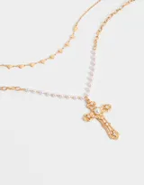 Collar doble dorado, uno con cadena de eslabones y dijes de corazones, y otro con perlas y dije de cruz con detalles de perlas.