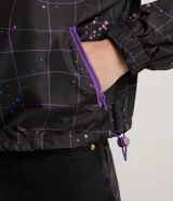 Campera cropped con capucha, de poliéster color negro con estampado de cuadros y salpicaduras de colores. Tiene cordón de ajuste en la capucha, elástico en puños y ruedo, bolsillos con cremallera y cierre frontal con cremallera.