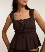 Blusa blanca con breteles anchos y escote cuadrado, detalle de lazo ajustable en el centro del busto y volado en el ruedo. El tejido es texturizado y ligero.