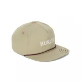 Gorra estilo trucker o snapback de color beige, con visera plana y cordón decorativo marrón cruzando el frente. Presenta el logo "HURLEY" bordado en blanco en el panel frontal.