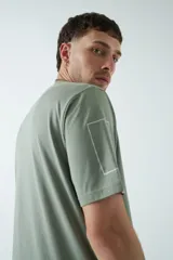 Remera verde militar de corte oversized, con cuello redondo y mangas cortas. Presenta un estampado con texto y figuras geométricas en el frente.