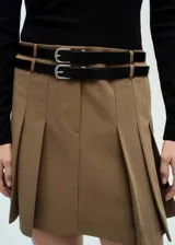 Minivestido marrón con falda plisada, doble cinturón de cuero sintético negro con hebillas plateadas, cuello alto, mangas largas y cierre lateral con cremallera.