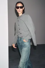 Chaqueta de punto color rosa pálido, con cuello redondo y cierre frontal de botones oscuros. Presenta mangas largas y un corte a la cintura.