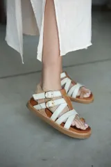 Sandalia de verano con tiras cruzadas de cuero en tono tostado y detalles en dorado.