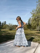 Vestido largo blanco con estampado floral azul, de estilo bohemio, con tirantes finos y volantes en el cuello.
