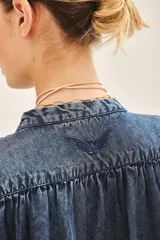Camisa celeste de corte amplio, con mangas cortas y cuello redondo. Confeccionada en tencel, con cartera oculta en el delantero y botones metálicos con el logo de la marca.