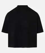 Remera de manga corta, cuello redondo y corte boxy, confeccionada en gamuza sintética (suede) de color negro. Presenta una pequeña estampa localizada en el pecho con un diseño abstracto en tonos dorados/bronce.