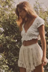 Top crop blanco de escote cuadrado y manga corta abullonada. Detalle de lazada en el pecho y volantes en el escote y el bajo.