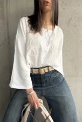 Blusa blanca de manga larga acampanada con bordado floral en el frente y cierre con botones.