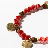 Pulsera elástica con cuentas facetadas de cristal rojo, cuentas doradas y cuentas de madera color marrón. Incluye dijes circulares dorados.