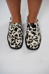 Mocasín de cuero con estampado animal print de vaca en tonos marrón y blanco, con capellada enrejillada y suela plana con plataforma delantera y taco bajo.