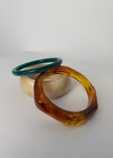 Set de tres pulseras rígidas de diferentes colores y materiales: una verde lisa, una beige con efecto marmolado y una color ámbar facetada.