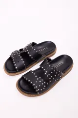 Sandalia tipo mule de mujer, color dorado metalizado, con dos tiras anchas superpuestas con borde festoneado y tachas doradas. La suela es gruesa y de color marrón claro.