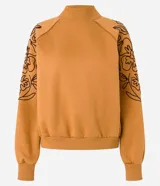 Sweater color ocre con cuello alto y mangas largas con sisas raglán. El sweater tiene bordados de flores en los laterales de las mangas.