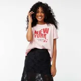 Camiseta rosa de corte amplio con estampado de texto en rojo que dice "New York, Sleepless Nights and City Lights" y dos estrellas.