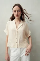 Camisa color crema de manga corta con cuello solapa y botones de nácar al frente, confeccionada en un tejido liviano de sutil textura.