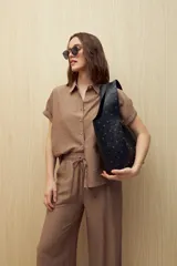 Camisa color marrón claro, de manga corta con puños arremangados, cuello clásico y cierre frontal con botones.