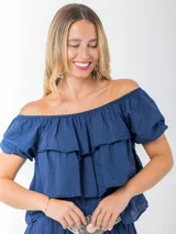 Blusa azul marino de algodón italiano, con escote elastizado que permite usarla con los hombros al descubierto o como remera con hombro abullonado. Presenta volados y mangas cortas abullonadas.