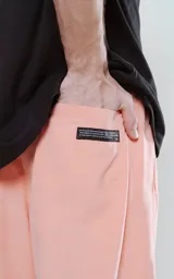 Pantalón de corte sastrero color salmón, de tela suede suave y holgada, con bolsillos laterales, cintura trasera elástica ajustable y cierre frontal con botón.