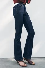 Pantalón de jean azul oscuro, de tiro medio, corte bootcut y largo hasta el tobillo. Tiene cinco bolsillos, trabillas en la cintura y cierre frontal con cremallera y botón metálico.
