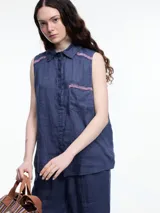 Camisa sin mangas negra de lino con cuello clásico, cierre frontal abotonado y bolsillo de parche en el pecho. Presenta bordados tipo pespunte en contraste en el frente y canesú trasero.