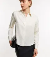 Camisa color crema en crepé con cuello solapa, abotonado frontal, mangas largas y textura de flores tramadas en el tejido.