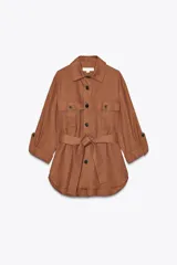 Camisa color marrón con cuello solapa y manga larga acabada en vuelta con trabilla y botón. Bolsillos delanteros de plastrón con solapa. Bajo con aberturas laterales. Cierre frontal con botones y cinturón de la misma tela.