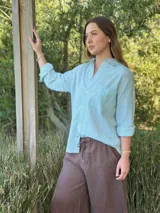 Camisa holgada a rayas verticales color beige y blanco, con cuello clásico, manga larga, bolsillo en el pecho y cierre frontal con botones nacarados.