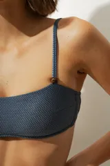 Top de bikini azul con textura, corte recto, tirantes finos y detalle de cuentas de madera en los tirantes.