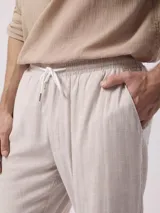 Pantalón largo de hombre, color beige con finas rayas verticales blancas, de corte recto y estilo pijamero.