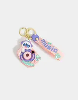 Llavero con forma de cámara de fotos rosada con detalles en lila y celeste. Incluye un dije con forma de conejo con auriculares y un strap con la palabra "music".