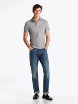 Chomba gris de algodón elástico con cuello y mangas ribeteadas en blanco y negro. Tiene cartera de tres botones, logo de Tommy Hilfiger bordado en el pecho y corte slim.