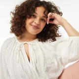 Blusa blanca con bordado calado, escote con lazo y mangas 3/4 abullonadas.