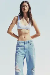 Pantalón de jean celeste claro, corte baggy, tiro medio, largo hasta el tobillo y con roturas grandes en ambas piernas.