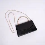 Cartera de mano tipo sobre color negro con textura símil cuero de reptil. Tiene manija rígida dorada y correa de cadena dorada desmontable.