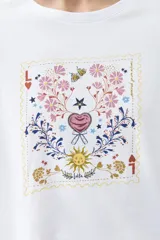 Remera blanca de algodón con cuello redondo y mangas cortas. Estampado rectangular con diseño floral y geométrico en tonos rojos, azules y amarillos.