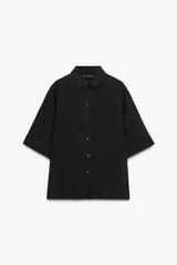 Camisa negra de manga corta confeccionada en hilatura con lyocell y ramio, con cuello solapa, bajo recto y cierre frontal con botones.
