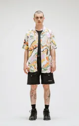 Camisa de manga corta con estampado de hojas en tonos naranja, verde y rosa sobre fondo blanco. Corte oversize.