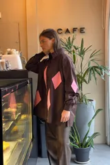 Camisa marrón con rombos rosas en el frente y en los codos, de corte recto y mangas largas.