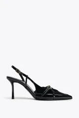 Zapato de tacón fino color negro charol, con punta fina, tiras cruzadas y hebilla ajustable en el tobillo.