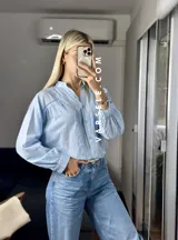 Camisa blanca de mangas largas con puños abullonados y detalles de encaje en cuello, mangas y ruedo.